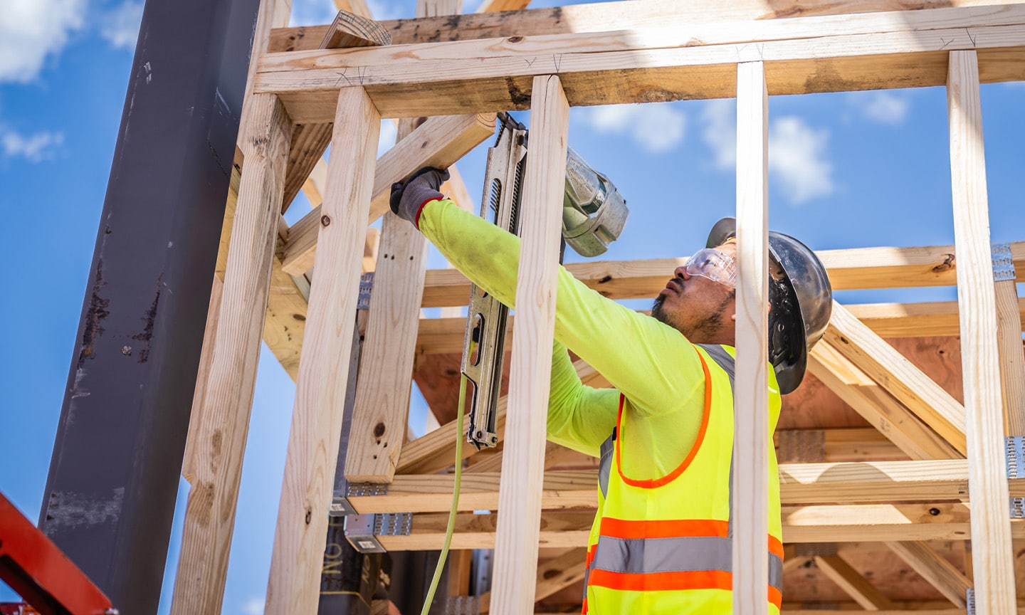 Man in safety gear using nail gun on wooden frame