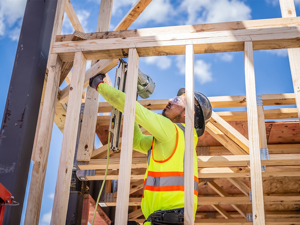Man in safety gear using nail gun on wooden frame